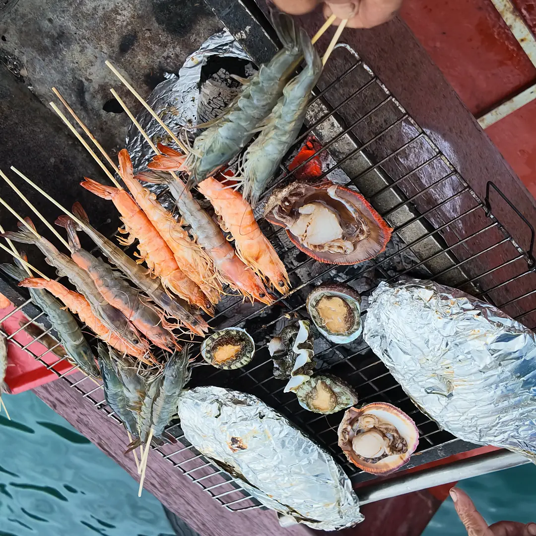 나트랑 선상 BBQ — 숯불 석쇠 위 새우 꼬치와 은박지에 싼 생선