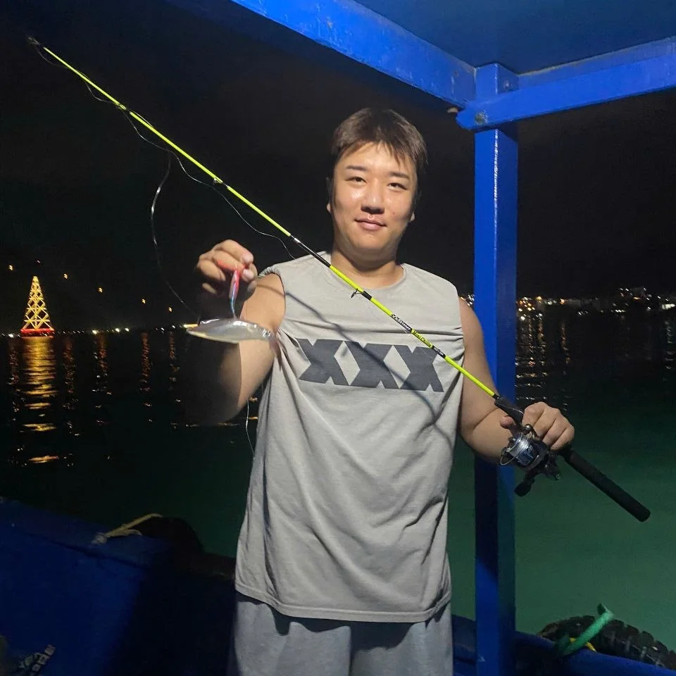 나트랑 야간 오징어 낚시 투어 — 낚싯대에 걸린 오징어를 들어 보이는 손님, 뒤로 레인보우 타워 불빛